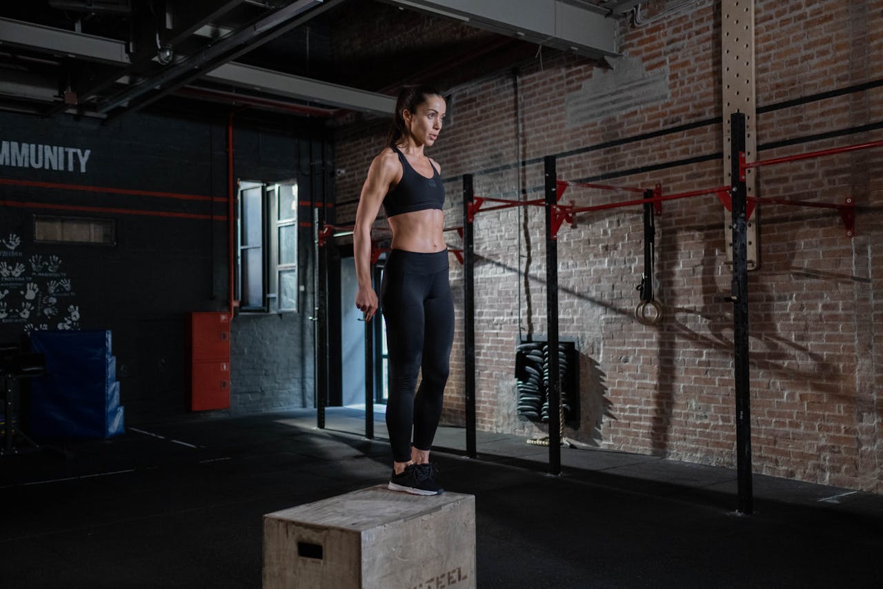 Fit woman performing a box jump in a gym, focused on fitness and strength training.